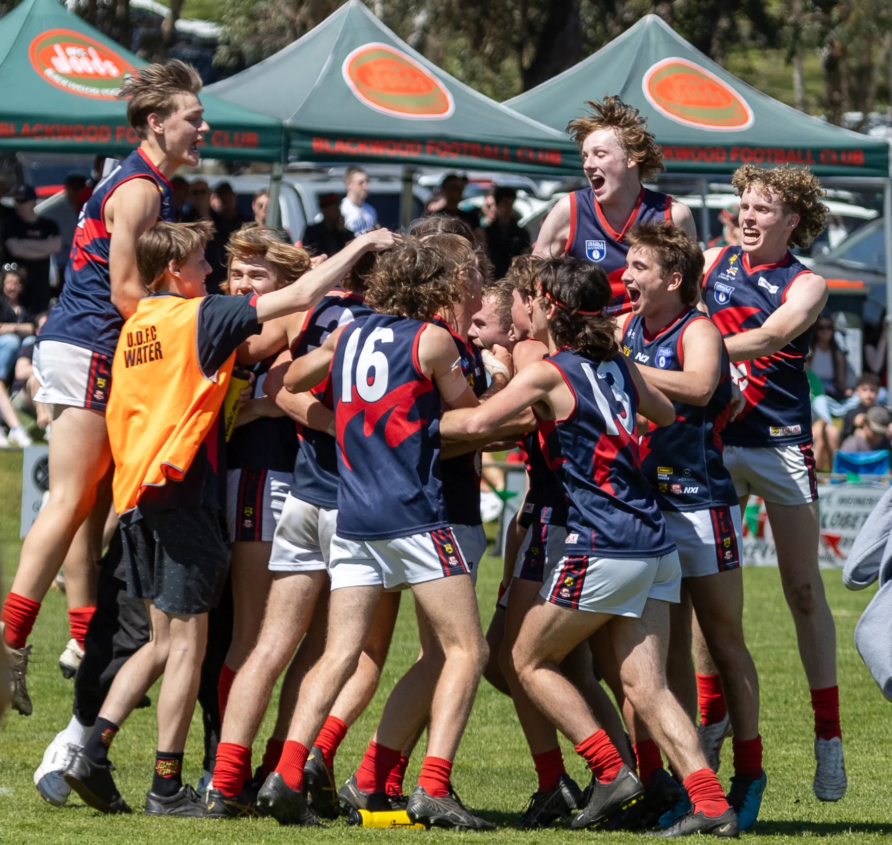 Uraidla Districts players in navy and red guernseys leaping into a huddle to celebrate